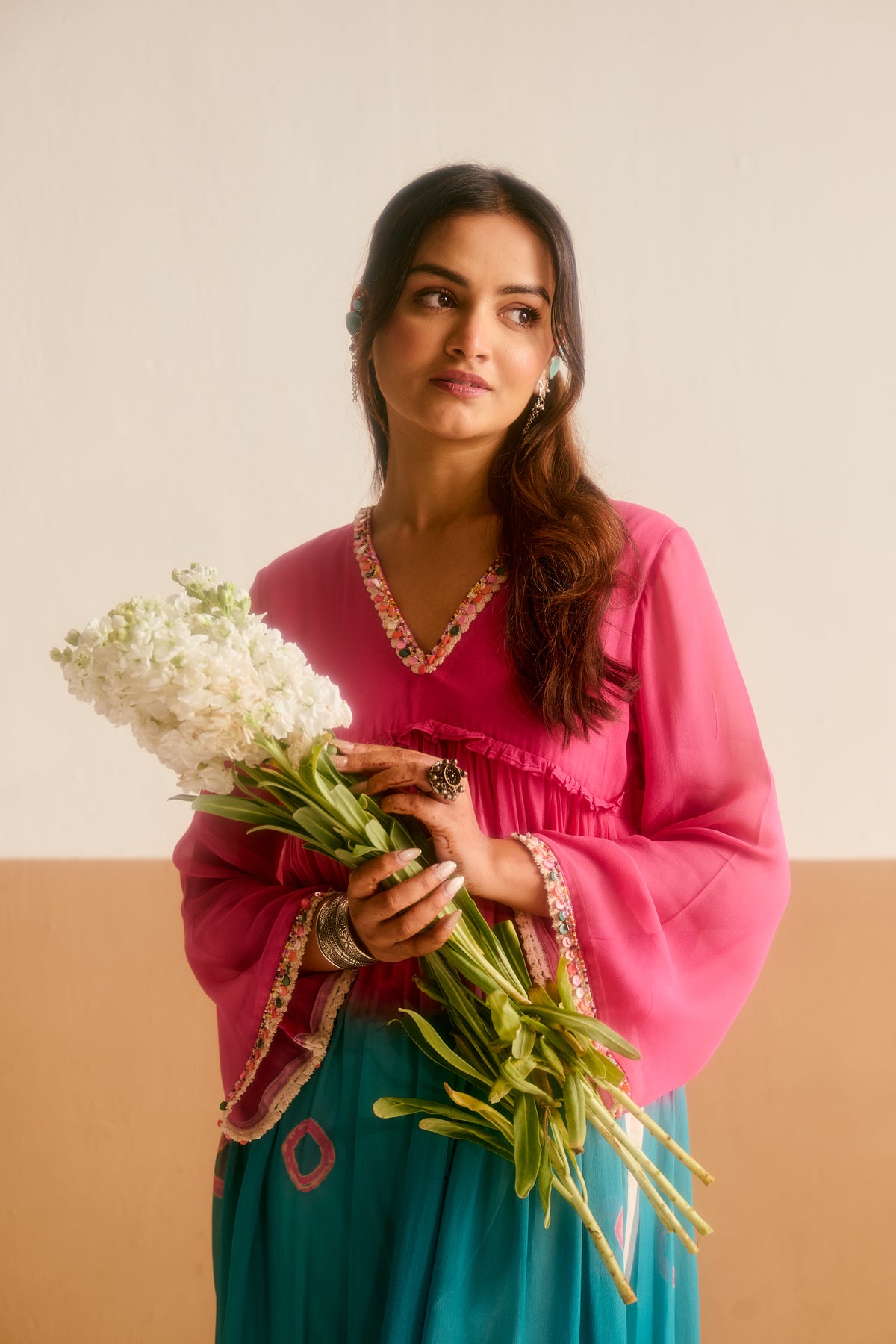 Woman holding a bouquet of flowers wearing a ombre tone kurta against a white and brown background