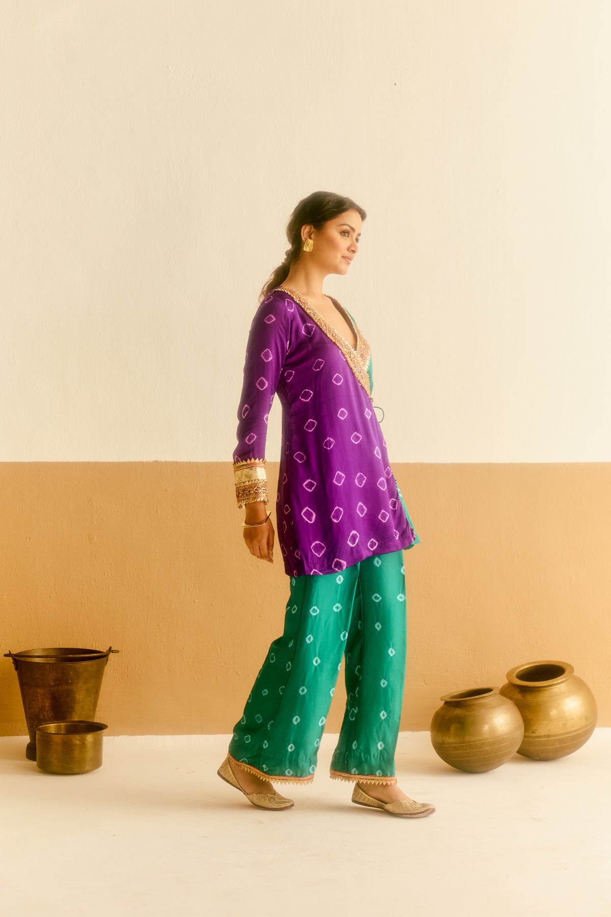 Woman wearing a purple and green hand tied and dyed top and green pants with a beige and brown background.